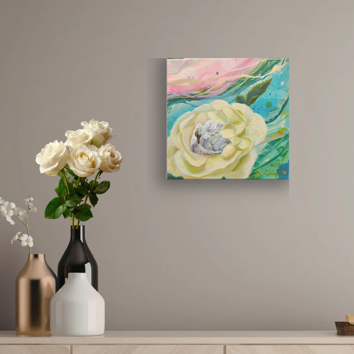 A square canvas wall art print featuring an abstract painting of a large cream-colored flower with green and pink brushstrokes, displayed on a gray wall above a console table with decorative vases and white roses.