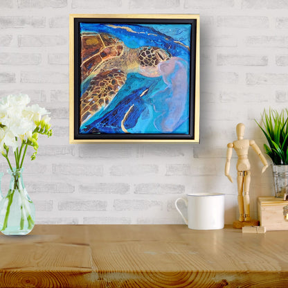 A framed abstract painting of a sea turtle hangs on a white brick wall above a wooden table with a vase of white flowers, a white mug, a small wooden figurine, and a potted plant.